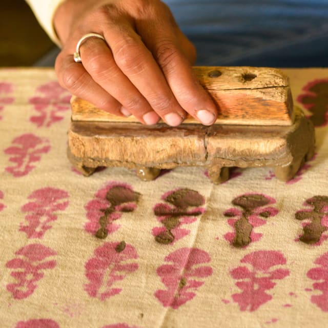 person using a block to print flower design onto fabric