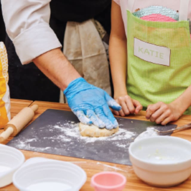 table with bowls and an adult working with dough as a kid watchs