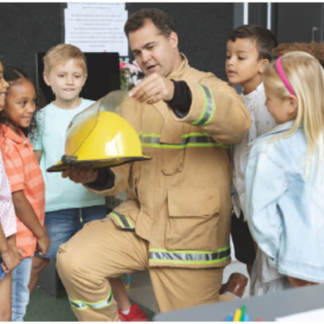 firefighter in uniform kneeling around group of kids