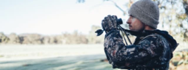 man dressed in camo with binoculars in a field