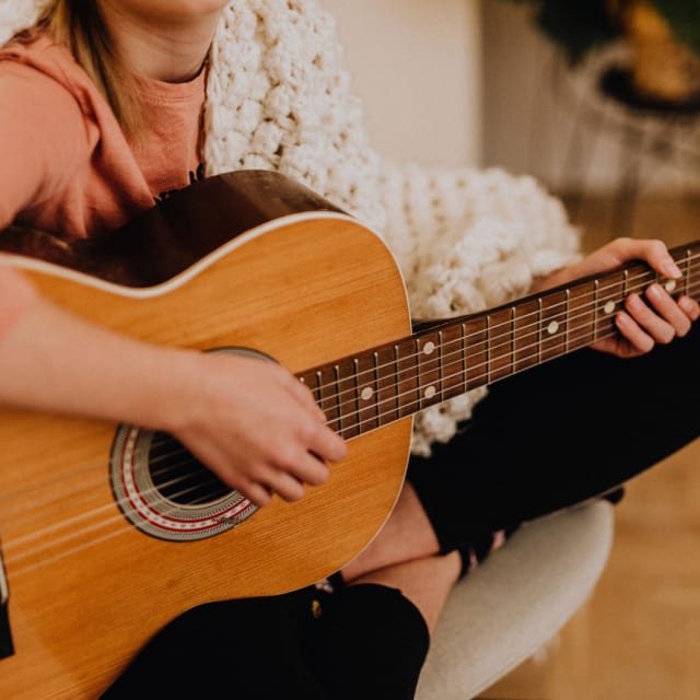 female playing a guitar in a comfy chair