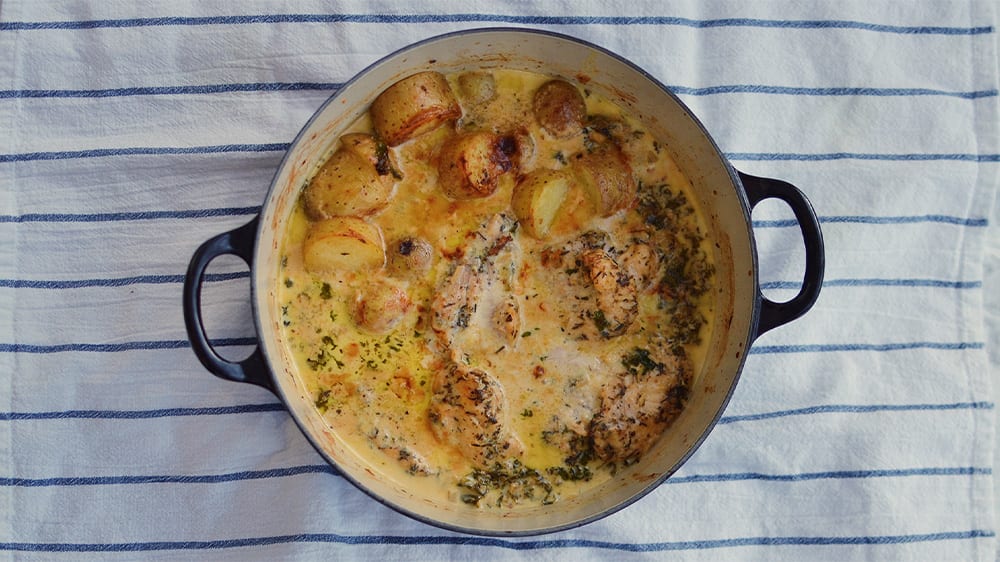 En kastrull med en dijonkyckling-gryta med potatis står på en randig kökshandduk.