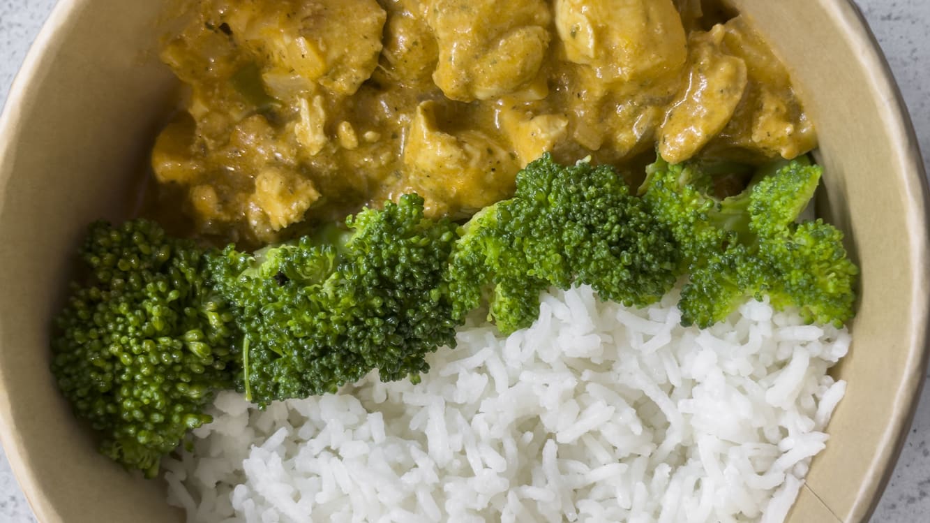En skål med currykyckling, ris och broccoli.