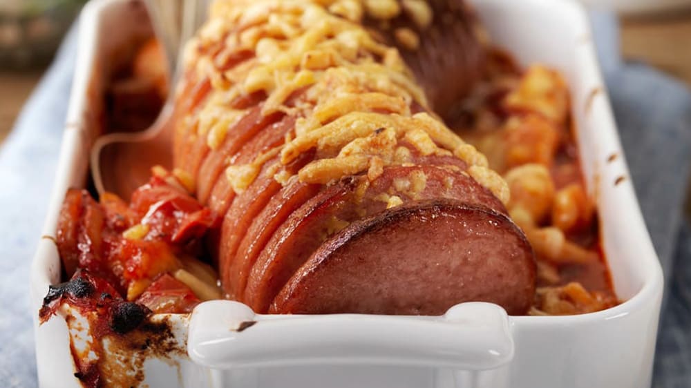 Skivad falukorv toppad med ost i en vit ugnsform.