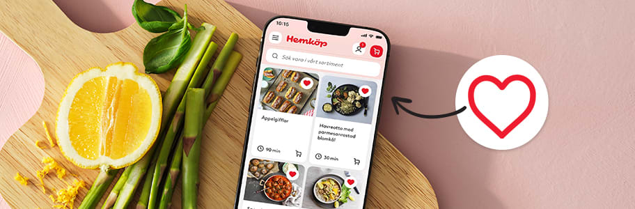En mobiltelefon med Hemköps hemsida på displayen med recept som markerats den ett ifyllt hjärta samt en pil riktad mot recepten med ett oifyllt hjärta, ligger på en skärbräda med färsk sparris och en delad citron.