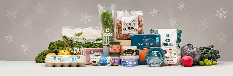 Ett bord med olika förpackningar med julvaror står grupperade så som färsk grönkål, färsk dill, färdiga köttbullar, en äggkartong, en påse potatis, romsås, räkor i lag, matjessill, prinskorv m.m.