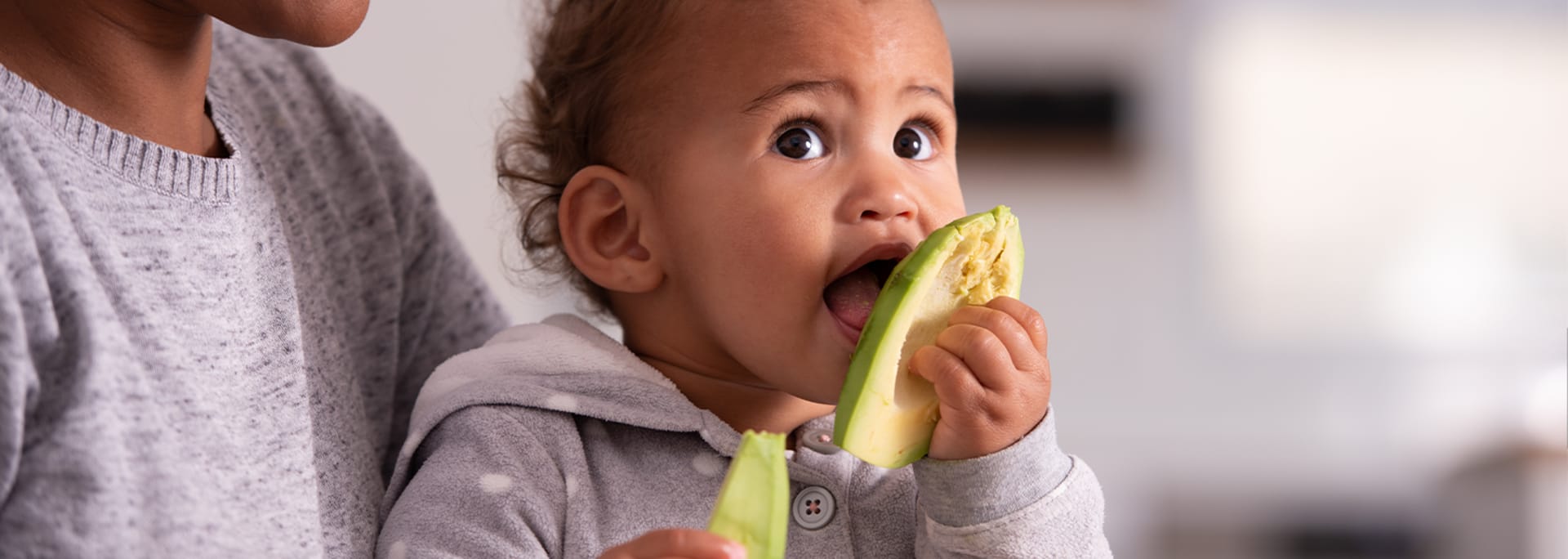 Baby sidder på skødet af mor og spiser avocado