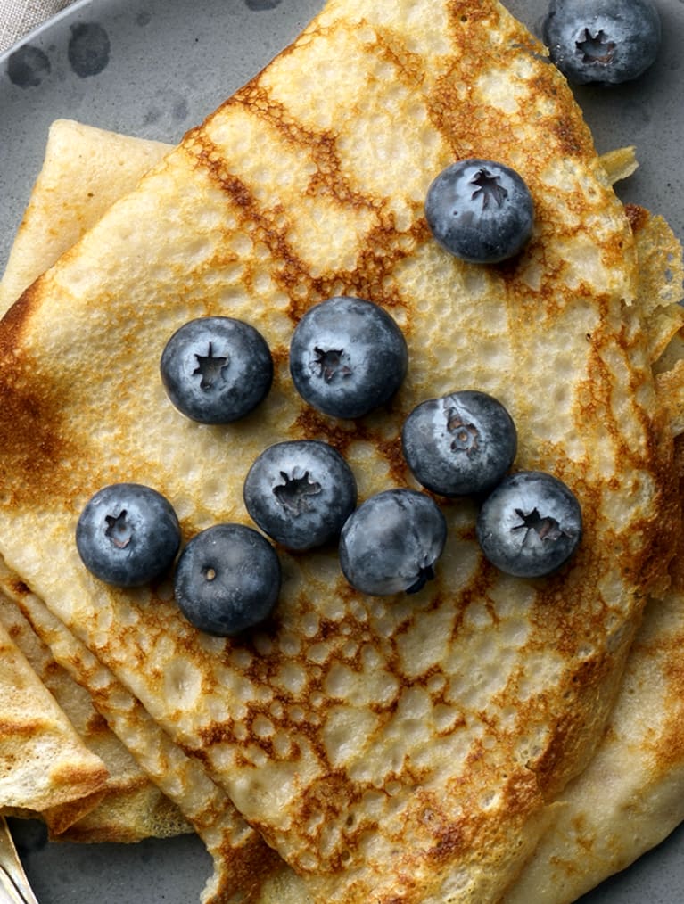 Två vikta glutenfria pannkakor på en en blå tallrik, toppade med blåbär