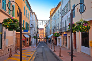Pedestrian street in Antibes Old Town with pastel façades, shutters, flower baskets and boutique shops.