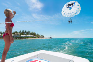 Parasail Crew member standing on back of parasail boat while waving at couple parasailing with Fury in Key West with island in the background