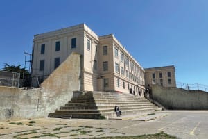 Historic beige institutional building with wide stone steps and barred windows under clear blue sky