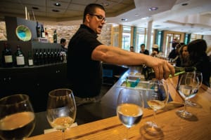 Wine tasting event with sommelier pouring white wine into glasses at a wooden bar counter