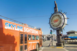 Orange Skyline Sightseeing tour bus at Fisherman's Wharf with iconic ship's wheel sign in San Francisco