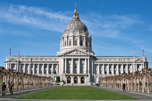 San Francisco City Hall with its iconic white dome and neoclassical architecture, flanked by palm trees and flags
