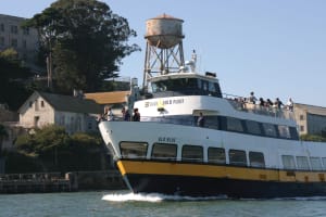 Blue and Gold Fleet ferry boat with passengers departing from a San Francisco Bay pier near historic buildings