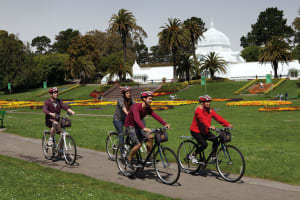 Group of cyclists riding bikes on a path in front of the Conservatory of Flowers in San Francisco's Golden Gate Park