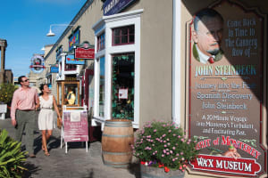 Couple walking past Bargetto Winery and Spirit of Monterey Wax Museum in Cannery Row with flowering planters