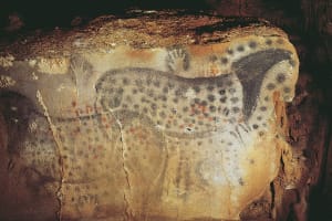 Prehistoric spotted horse paintings with hand stencils on a stone wall inside Pech Merle cave in the Lot region of France.