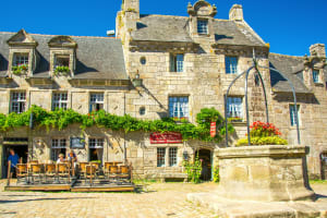 Historic stone houses and café terrace around the main square in Locronan with old well.