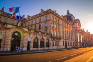 Musée d’Orsay exterior in Paris, with an ornate stone façade, French flags and golden sunlight illuminating the street.