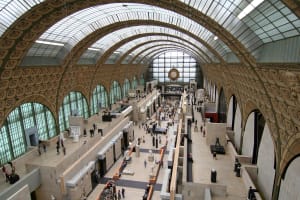 Elevated view of the Musée d’Orsay’s main hall, with sculptures, visitors and exhibition galleries beneath a vaulted glass roof.