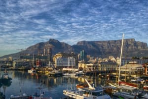 A photo taken across the harbour basin at the Victoria & Alfred Waterfront, showing boats and buildings, with Table Mountain in the background.