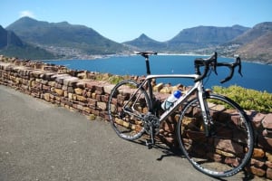 Photo of a road bicycle leaning against the stone wall at the Chapman's Peak lookout with views of the bay of Hout Bay in the background.