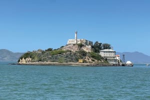 Alcatraz Island with lighthouse and prison buildings surrounded by turquoise bay waters and distant hills