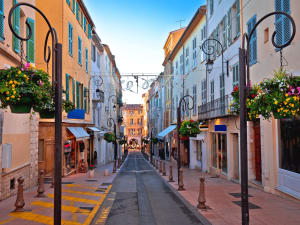 Pedestrian street in Antibes Old Town with pastel façades, shutters, flower baskets and boutique shops.