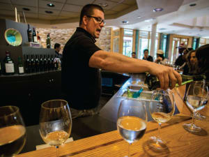 Wine tasting event with sommelier pouring white wine into glasses at a wooden bar counter