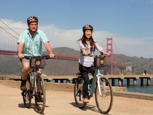 Two cyclists with helmets and bike bags pose in front of the Golden Gate Bridge in San Francisco