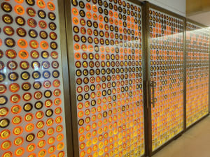 Floor-to-ceiling display of hundreds of gold and amber Château d'Yquem bottle caps mounted on illuminated glass panels inside the château