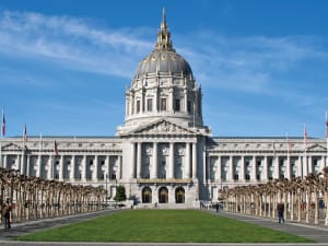 San Francisco City Hall with its iconic white dome and neoclassical architecture, flanked by palm trees and flags