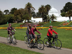Group of cyclists riding bikes on a path in front of the Conservatory of Flowers in San Francisco's Golden Gate Park