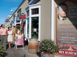 Couple walking past Bargetto Winery and Spirit of Monterey Wax Museum in Cannery Row with flowering planters