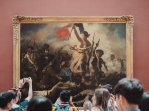 Visitors gathered in front of a large framed painting at the Louvre Museum