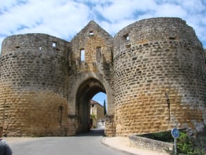 Massive twin stone towers forming a medieval gateway into the village of Domme in the Dordogne, France, under a partly cloudy sky