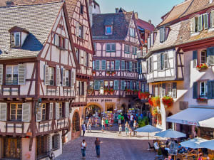 People walking in Obernai’s cobbled square surrounded by half‑timbered houses and cafés