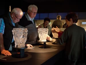 Group of adults examine illuminated Lalique crystal vases in a gallery