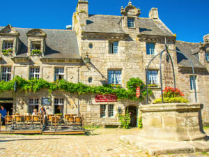 Historic stone houses and café terrace around the main square in Locronan with old well.