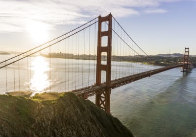 Golden Gate Bridge spanning San Francisco Bay with rocky coastline in foreground and city skyline visible in background