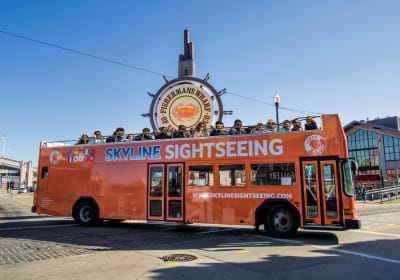 Orange double-decker Skyline Sightseeing tour bus with passengers on open-air upper deck near waterfront
