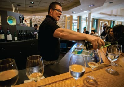 Wine tasting event with sommelier pouring white wine into glasses at a wooden bar counter