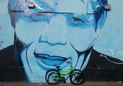 Photo of a bicycle standing next to a wall that is painted with an enormous street-art image of Nelson Mandela's face.