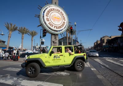 Tour passing the Fishermans Wharf Crab Wheel sign in an open top Jeep 