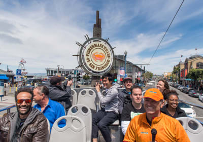 Tourists on a cable car at Fisherman's Wharf with the iconic ship's wheel sign visible in San Francisco