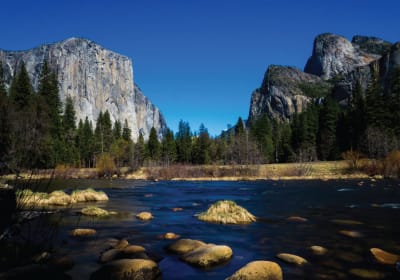 El Capitan and Three Brothers rock formations frame the Merced River in Yosemite Valley with evergreen forest