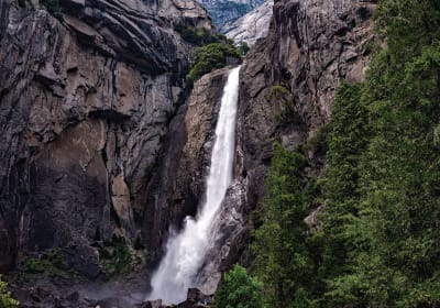 Tall waterfall cascading down rocky cliff surrounded by lush green vegetation in a mountain gorge