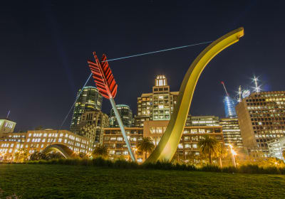 Illuminated modern sculpture installations in urban park at night with city skyline backdrop