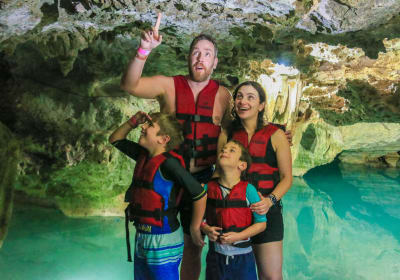 Family exploring a crystal-clear cenote inside a limestone cave in the Riviera Maya, Mexico.